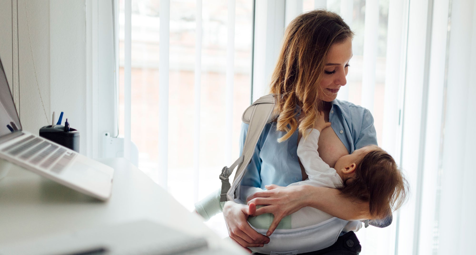 Working mom in office is nursing her baby in Pick-Me-Up nurse sling