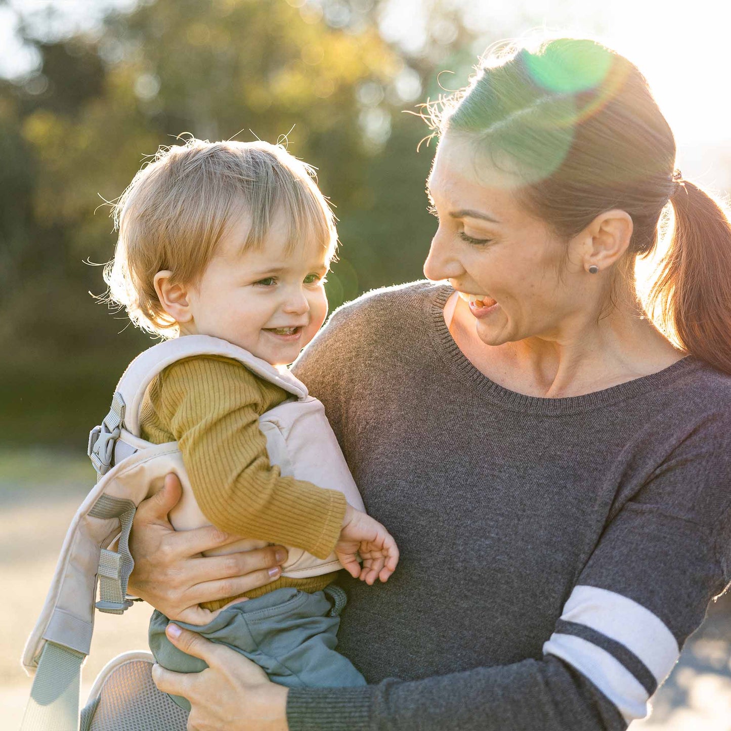 Mother laughing with baby in her arm and baby has a soft baby walker on